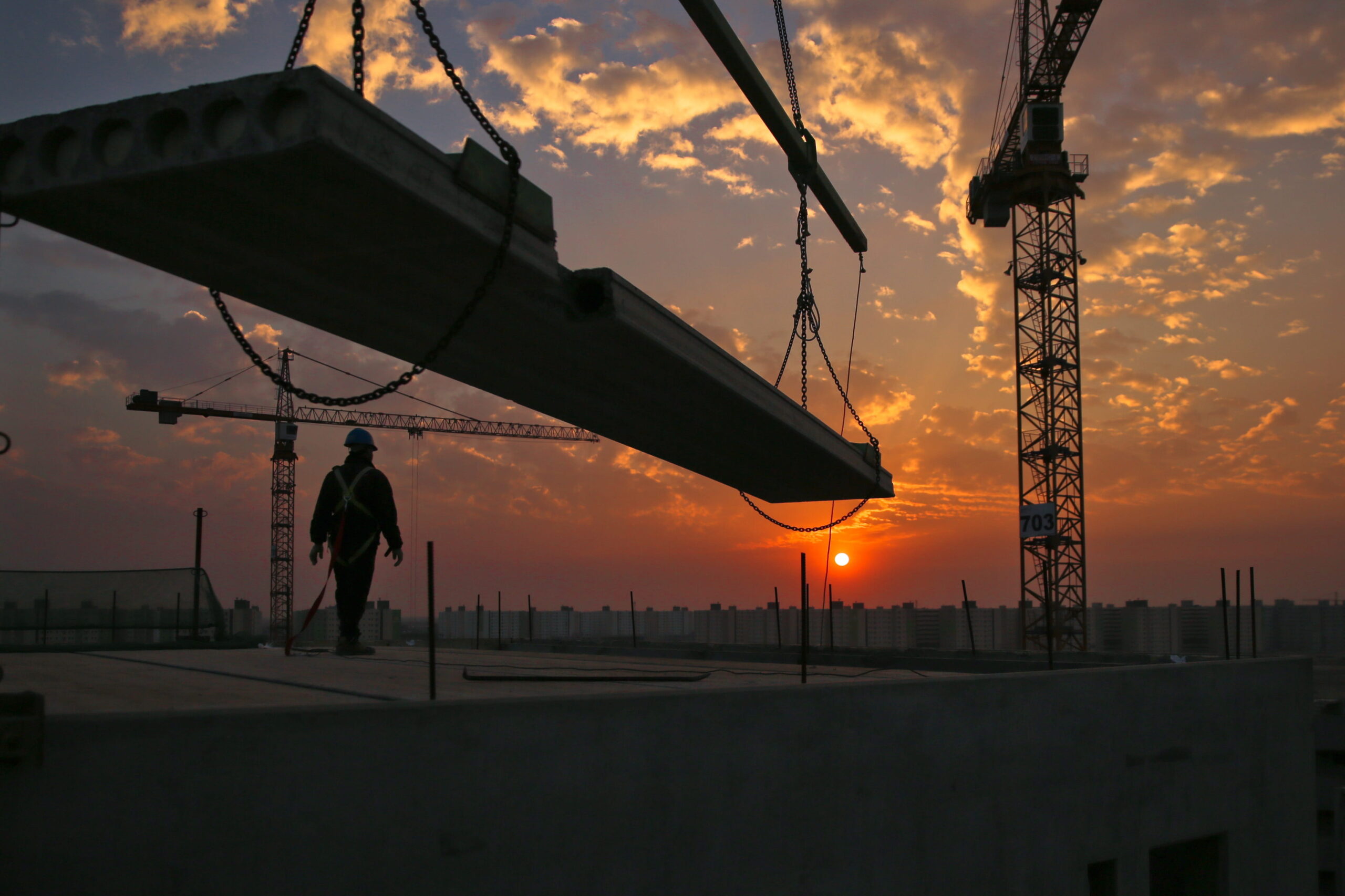 About landing page feature and header image. Photograph is of a construction worker on top of a building viewing a beautiful sunset with a crane in the frame.